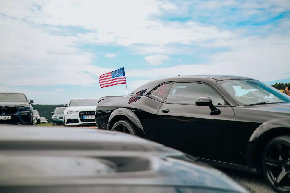 Černý Dodge Challenger s americkou vlajkou, v popředí další vůz