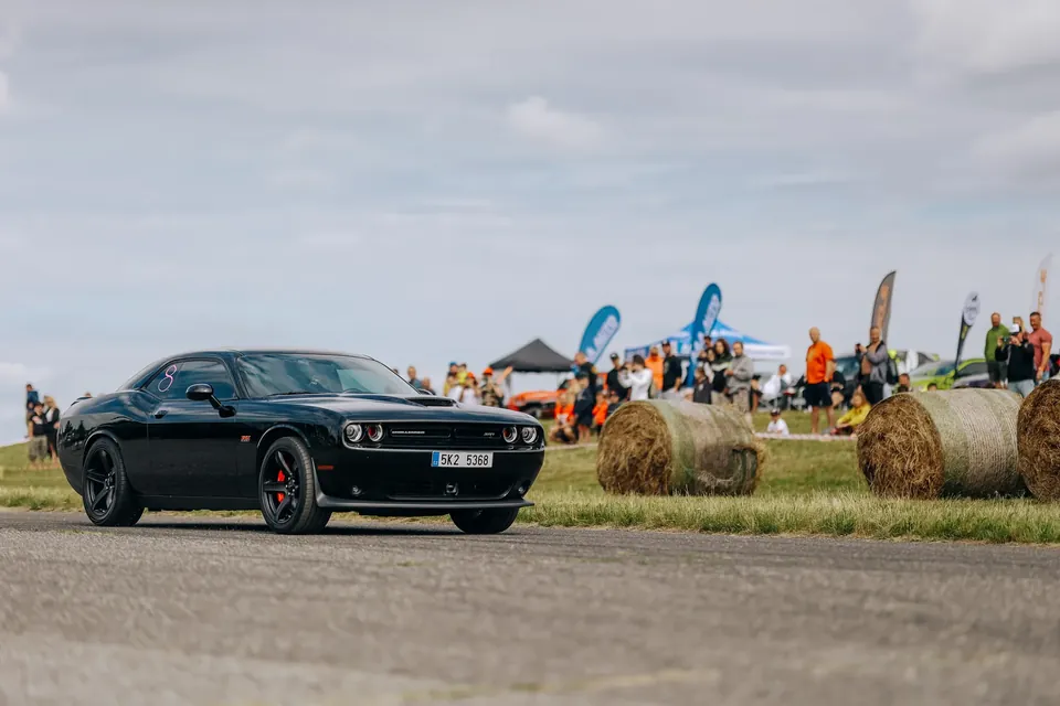 Černý Dodge Challenger na dráze, vedle balíky slámy a diváci