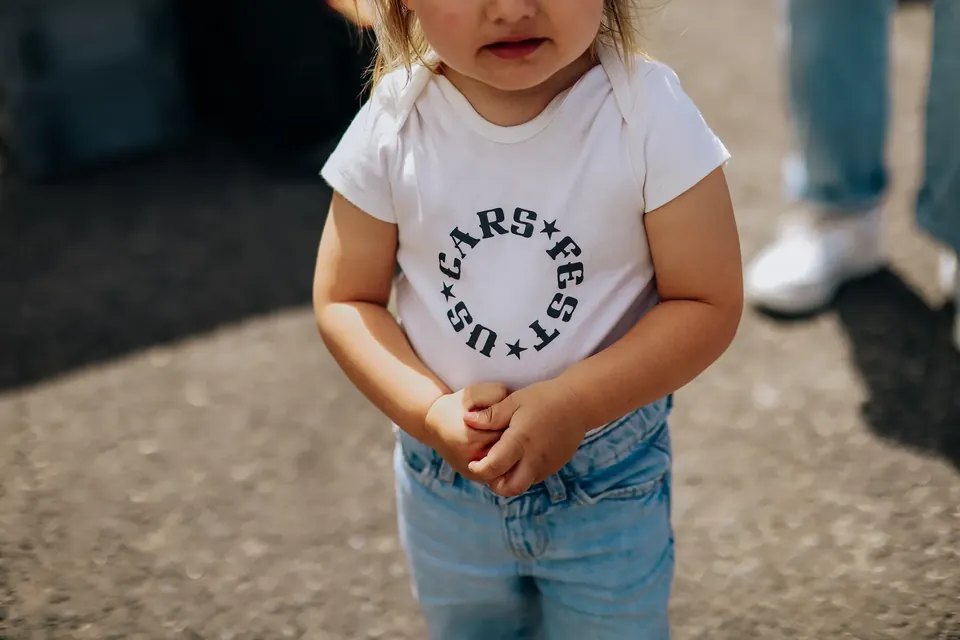 Malé dítě v bílém tričku s nápisem US Cars Fest