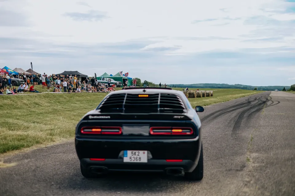 Černý Dodge Challenger SRT zezadu na dráze, v pozadí stany a diváci na svahu