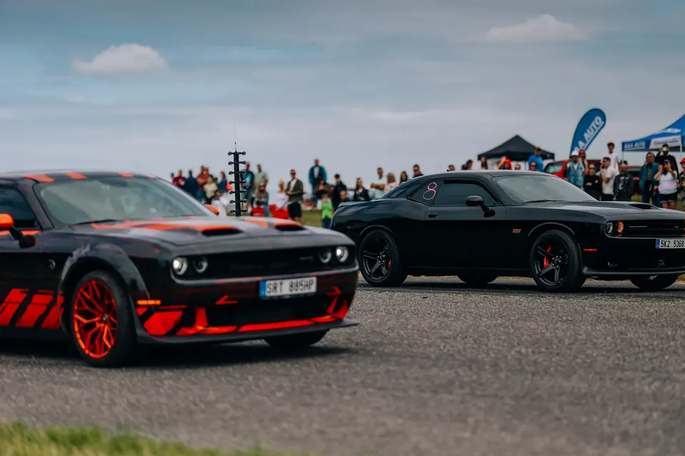 Dodge Challenger s červeno-černým polepem a černý Challenger na startu