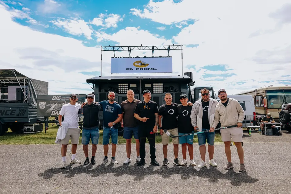 Skupina mužů pózuje před pódiem a technikou na US Cars Fest